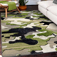 Load image into Gallery viewer, Ambush Zone in Green rug styled in a living room with white sofa and rattan chair—camo pattern adds gamer edge to cozy interiors
