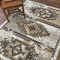 Load image into Gallery viewer, The Driftmarch Rug with a rustic chair placed on top, showing its tribal pattern and desert-toned palette in a cozy, frontier-inspired space