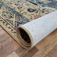 Load image into Gallery viewer, Rolled corner of the Ingenue rug from Area of Effect, showing Lok-Bak™ backing, surged edge, and intricate fantasy pattern on hardwood floor.