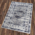 Load image into Gallery viewer, The Mistrender’s Medallion rug placed on a wooden floor, showcasing its faded medallion pattern in muted navy, gray, and ivory tones with soft vintage texture