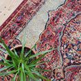 Load image into Gallery viewer, The Oathforged Rug styled with a leafy potted plant resting on top, adding natural contrast to its regal patterning