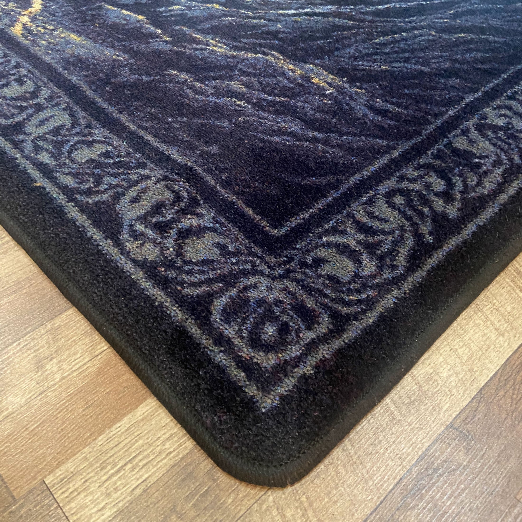 Close-up of the corner of the Silent Watch fantasy game room rug, showing plush texture and detailed border pattern on a hardwood floor.