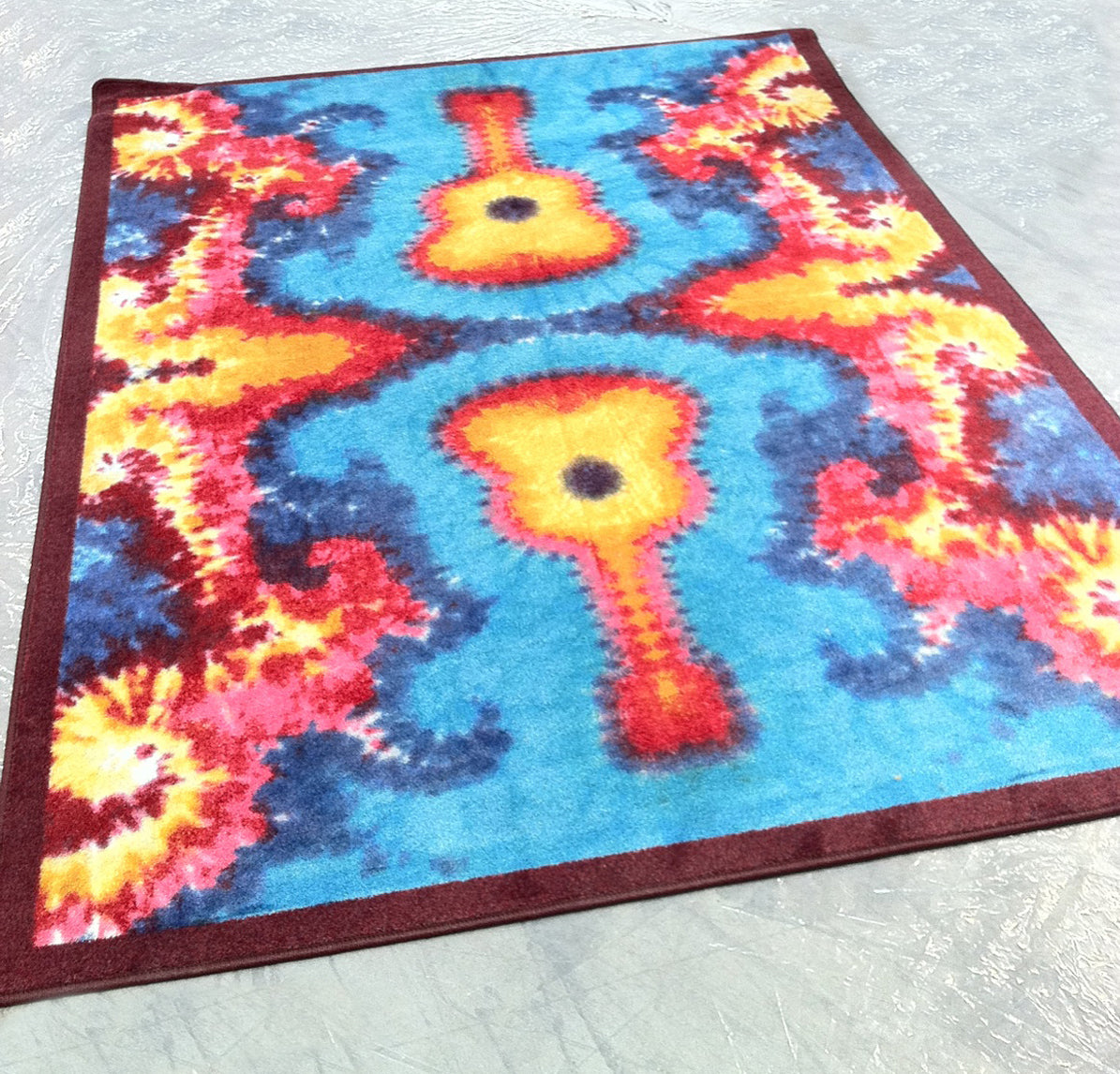 Strummoner tie dye guitar rug displayed in a room with a plastic-style floor, shown at an angle—adds bold color and musical flair to gamer or creative spaces