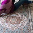 Load image into Gallery viewer, Tighter lifestyle shot of a girl leaning against The Weaver’s Medallion rug, showing the floral medallion and artisan details up close