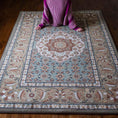 Load image into Gallery viewer, Lifestyle photo of a girl leaning back against The Weaver’s Medallion rug, showcasing its soft sage and parchment design with delicate floral medallion details