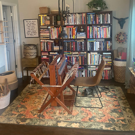 Room with bookshelves filled with books, a chair, and decorative items on a patterned rug.