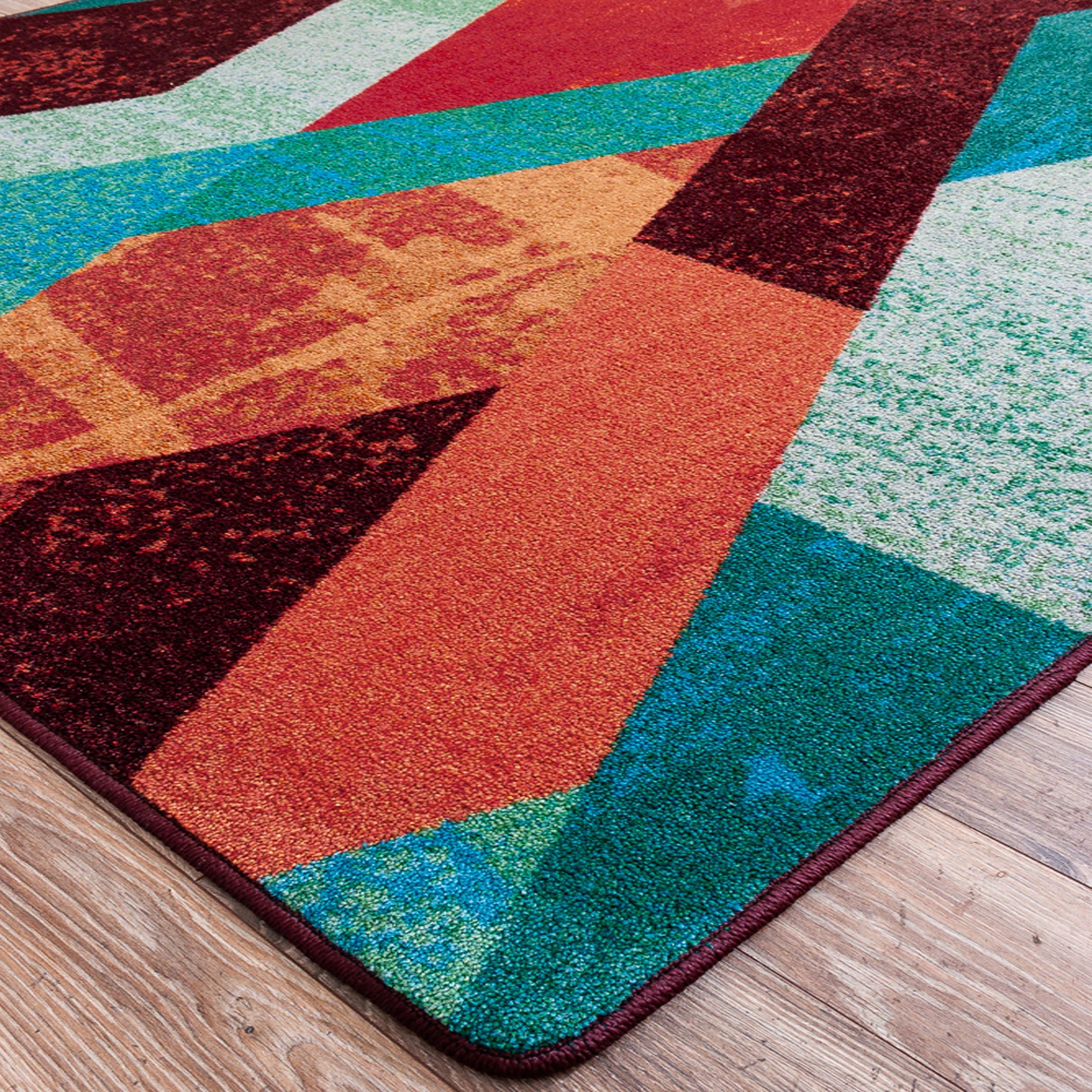Close-up of The Jester’s Tune rug corner showing vibrant layered diamond shapes in bold jewel tones with a slightly distressed texture

