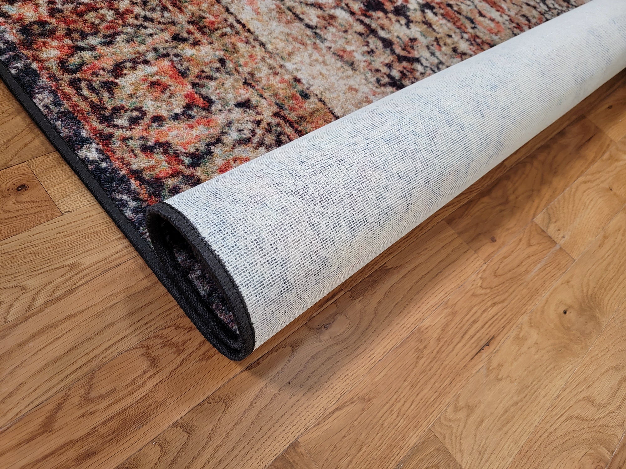 The Ravencourt Rug rolled to display the sturdy backing and weathered crimson tones in vintage elegance.