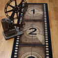 Load image into Gallery viewer, Reel Time rug styled with a vintage film projector, showcasing its filmstrip countdown design in a retro home theater setup
