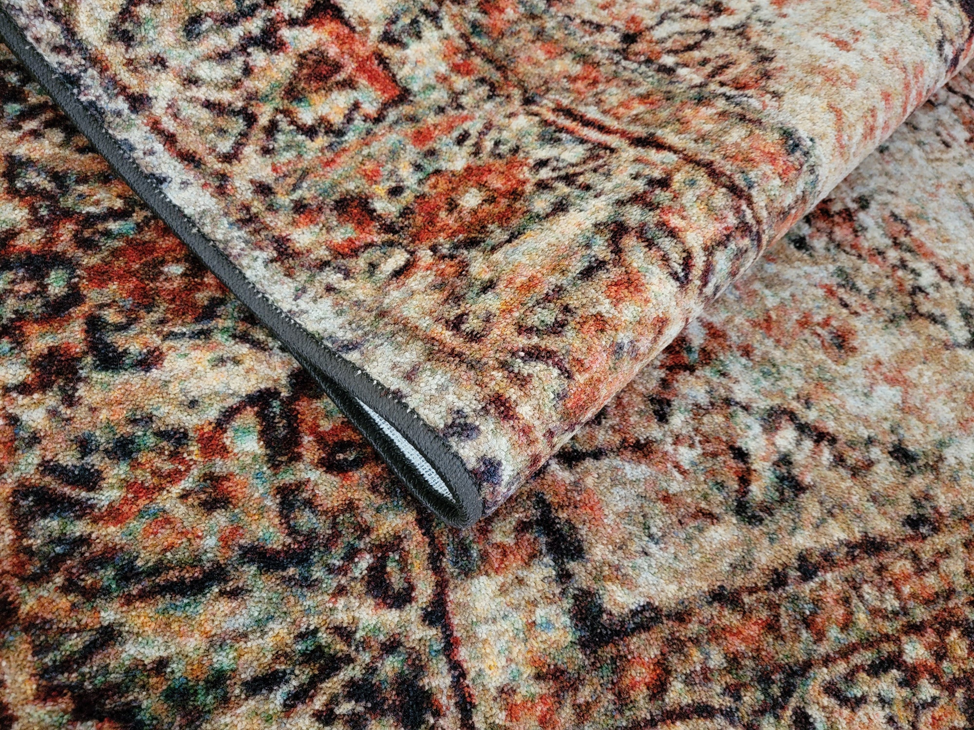 The Ravencourt Rug folded to reveal its durable construction and richly layered design of reds and ash black.