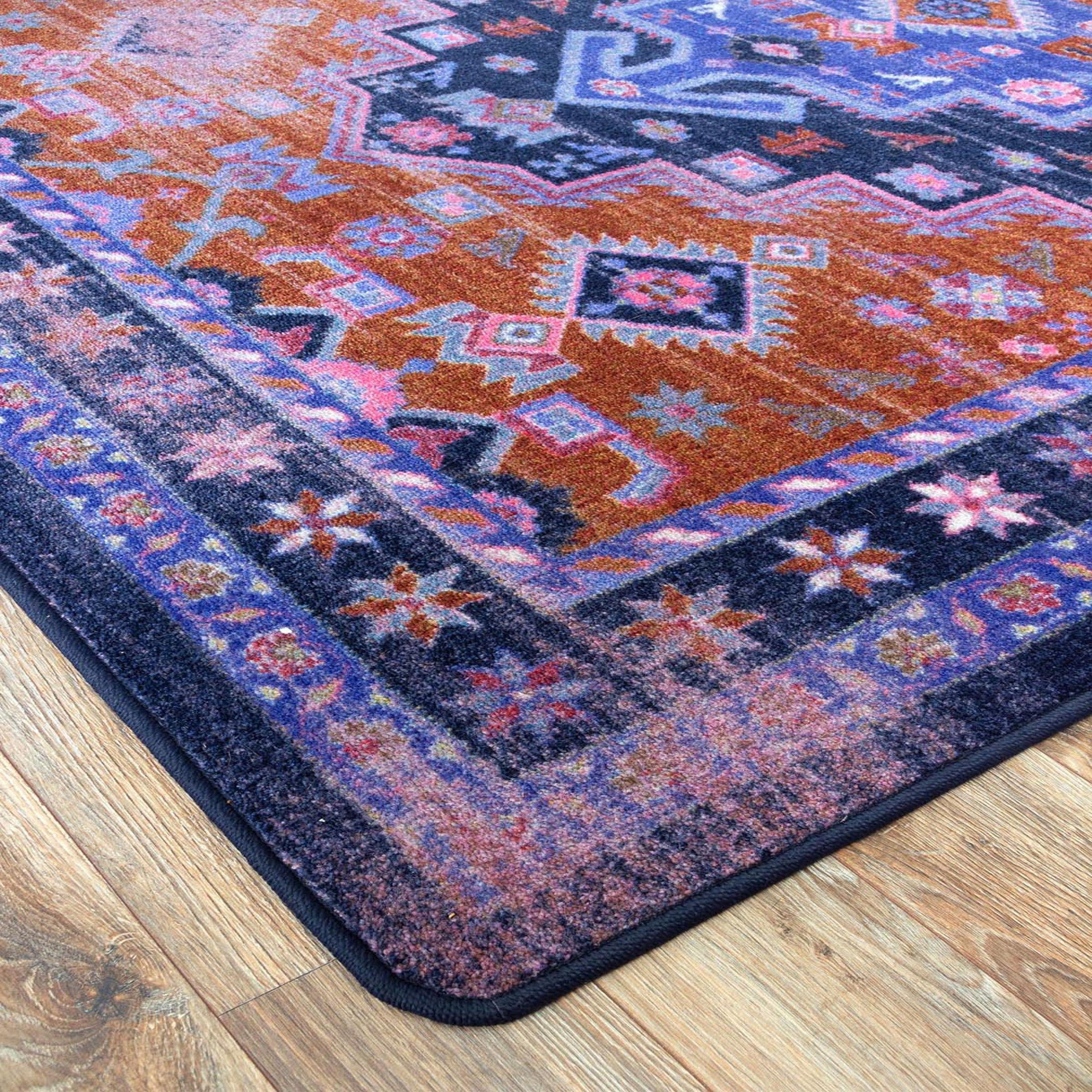 Close-up of the Twilight Caravan rug corner showing intricate geometric patterns in faded indigo, rust, and violet tones with detailed edging

