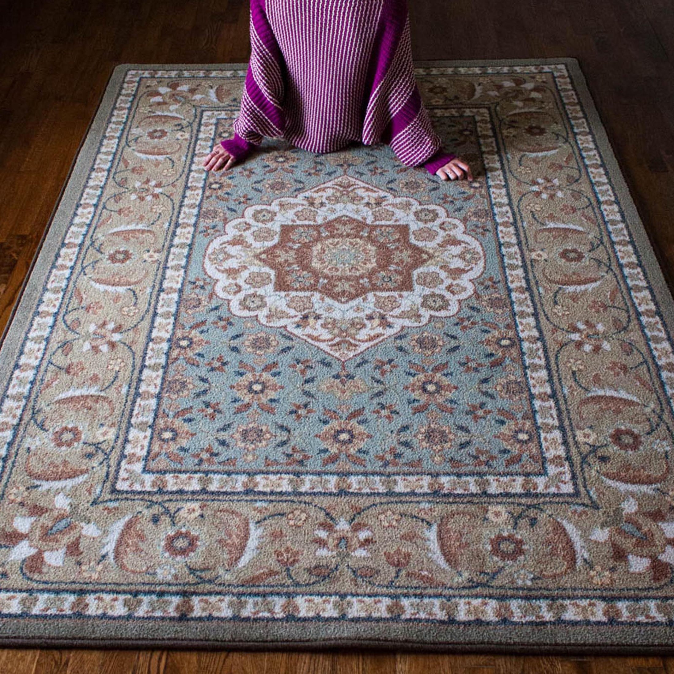 Lifestyle photo of a girl leaning back against The Weaver’s Medallion rug, showcasing its soft sage and parchment design with delicate floral medallion details