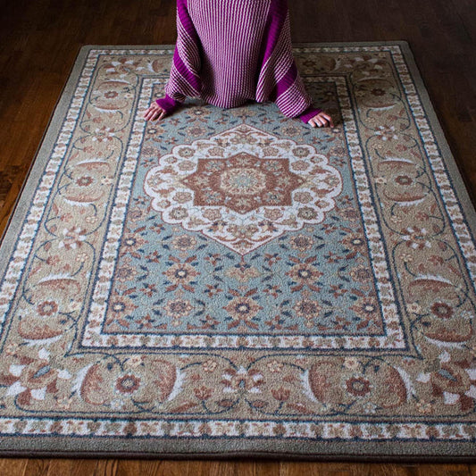 Lifestyle photo of a girl leaning back against The Weaver’s Medallion rug, showcasing its soft sage and parchment design with delicate floral medallion details